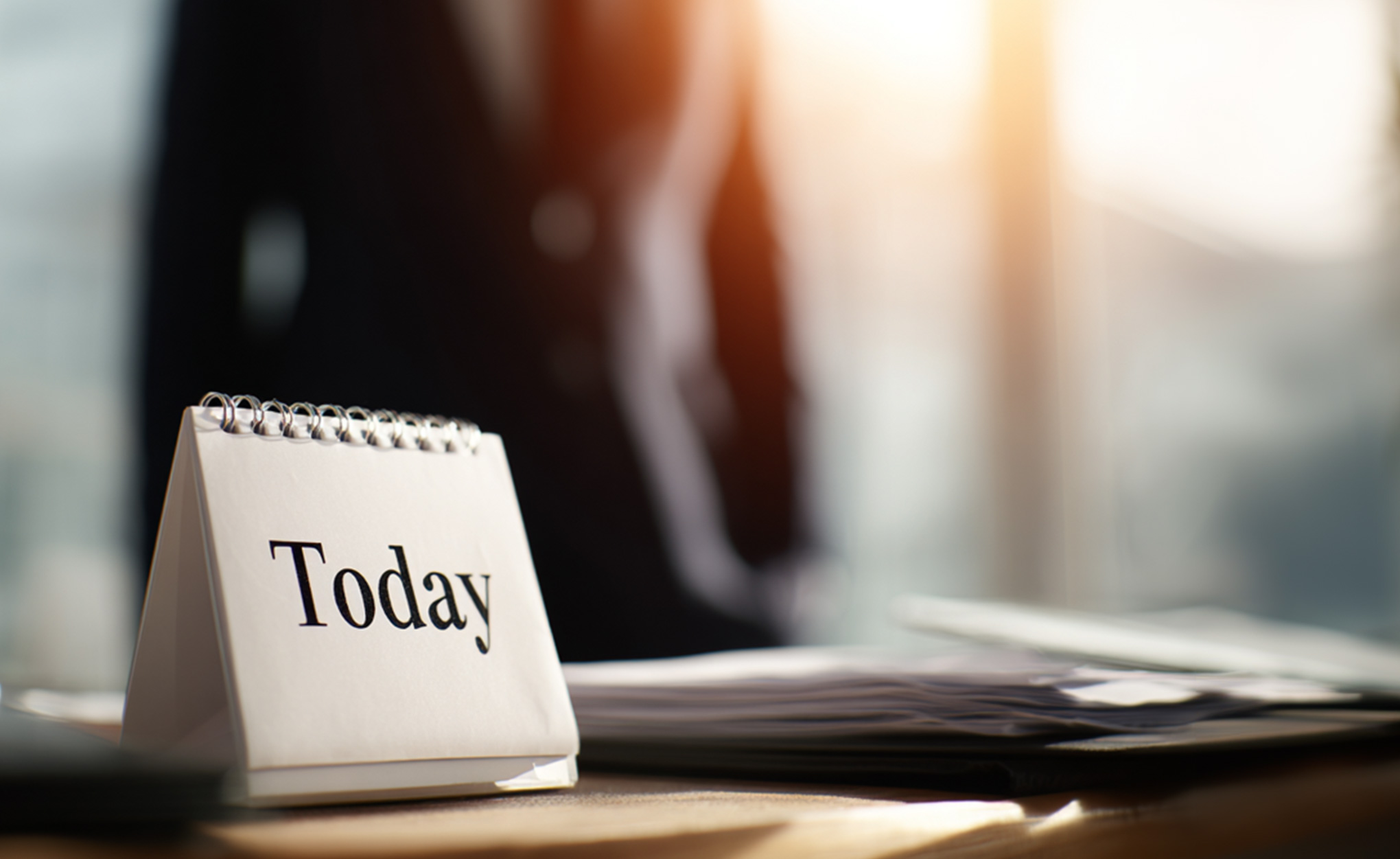 Das Bild zeigt einen Abrisskalender. Im Hintergrund verschwommen ein Geschäftsmann im Büroraum.